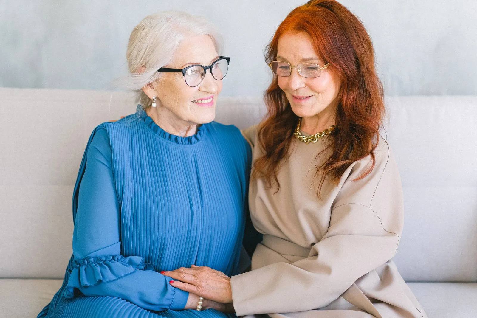 Two women sitting together on a sofa, smiling and holding hands.